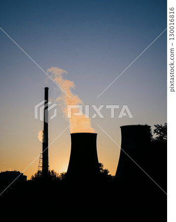 Industrial chimneys releasing large amounts of smoke and steam into atmosphere during sunset, symbolizing environmental pollution and climate change. Smoky industrial chimneys emitting thick plumes Industrial chimneys releasing large amounts of smoke and steam into atmosphere during sunset, symbolizing environmental pollution and climate change. Smoky industrial chimneys emitting thick plumes 130016816