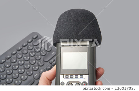 Hand holding portable audio recorder with microphone foam and wireless keyboard 130017053