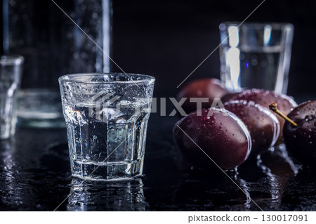 Distilled alcohol and plums on black table. Plum brandy shot. Distilled alcohol and plums on black table. Plum brandy shot. 130017091
