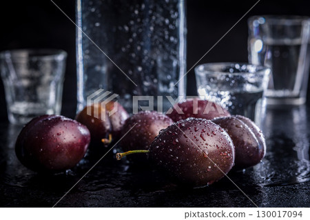 Plums and distilled alcohol on black table. Plum brandy shot. Plums and distilled alcohol on black table. Plum brandy shot. 130017094