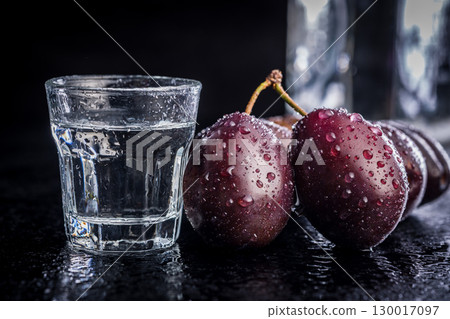 Plums and distilled alcohol on black table. Plum brandy shot. 130017097