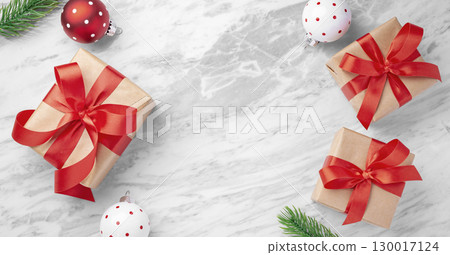 Christmas background, gift box with red bow ribbon with ball and leaves decor on marble table background, top view 130017124