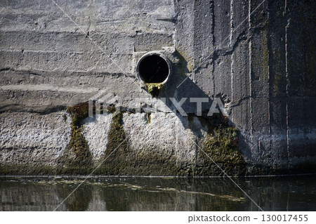 A concrete wall with a drainage pipe and water reflection 130017455