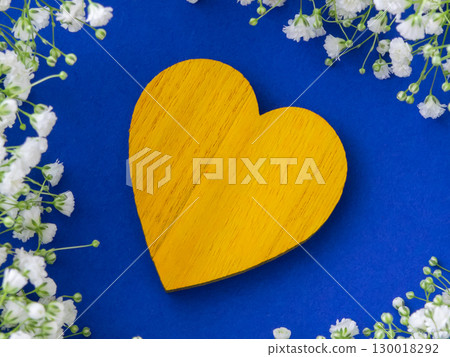 Beautiful yellow  wood heart on the fabric blau background between little white flowers. 130018292