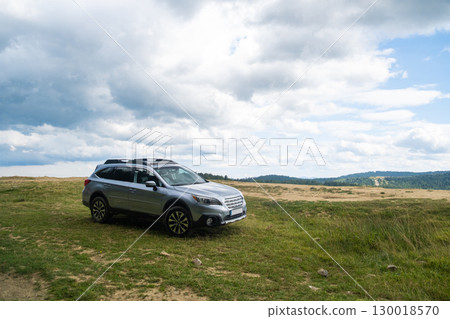 Silver SUV on Grassy Hill with Cloudy Sky Silver SUV on Grassy Hill with Cloudy Sky 130018570