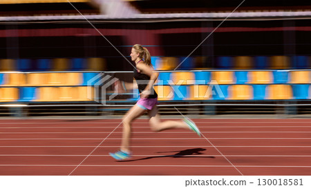 Woman sprinting on track with blurred background in vibrant stadium Woman sprinting on track with blurred background in vibrant stadium 130018581