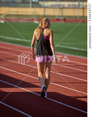 Woman athlete strolls on sunny track wearing sportswear for daytime practice Woman athlete strolls on sunny track wearing sportswear for daytime practice 130018727