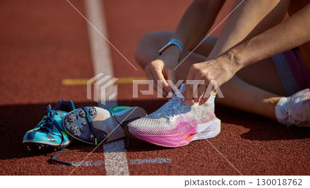 Runner tying shoelaces on athletic track with light blue shoes beside 130018762
