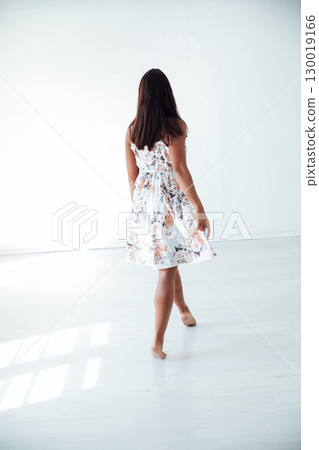 Tanned brunette woman in summer dress with flowers in white room 130019166