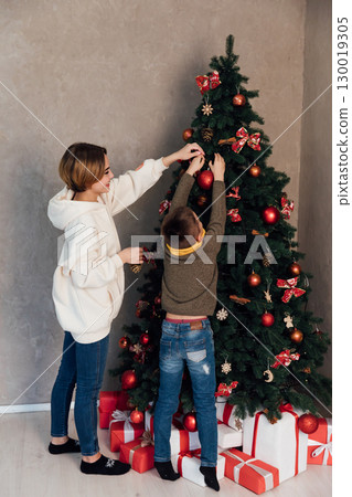 Mom and son decorating Christmas tree with gifts and toys 130019305
