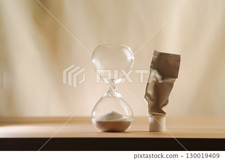 Hourglass with no time left and empty cream tube. Minimalist beige skincare aging concept Hourglass with no time left and empty cream tube. Minimalist beige skincare aging concept 130019409