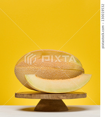 Half of a cantaloupe melon and a single slice placed on a white surface. Yellow background. Half of a cantaloupe melon and a single slice placed on a white surface. Yellow background. 130019532