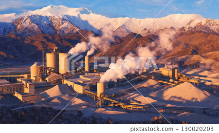 Industrial factory with smokestacks in mountainous landscape at sunset 130020203