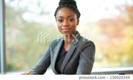Confident African female woman young adult professional in gray suit at office desk Confident African female woman young adult professional in gray suit at office desk 130020349