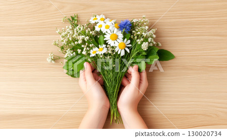 Child hands holding wildflower bouquet on wooden background 130020734