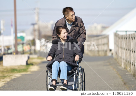 A husband taking a walk pushing his wife's wheelchair 130021180