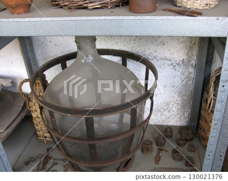 Large Glass Bottle Encased in Rustic Metal Cage on Workshop Shelf Display Large Glass Bottle Encased in Rustic Metal Cage on Workshop Shelf Display 130021376