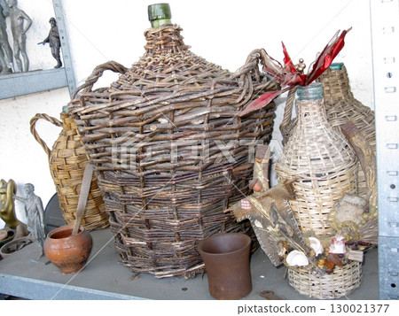 Collection of Woven Wicker Bottles with Clay Pots on Rustic Workshop Shelf 130021377
