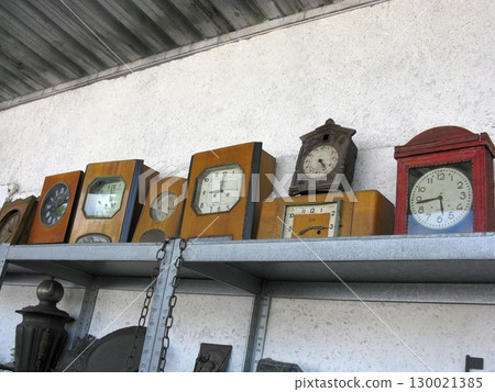 A row of vintage wooden clocks on a metal shelf, showcasing diverse designs and aged faces, reflecting the passage of time in a nostalgic antique setting 130021385