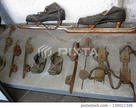 A collection of old ice skates and metal crampons arranged on a shelf, showcasing weathered leather and rusty metal, hinting at past winter adventures 130021386
