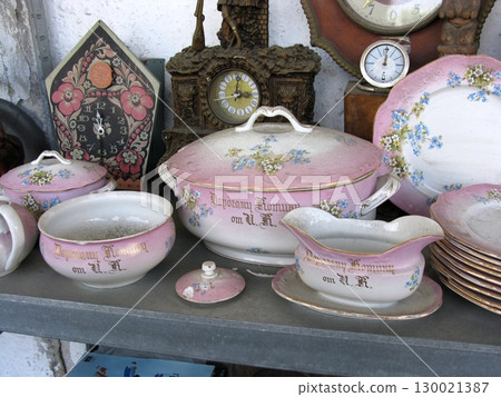 A set of vintage pink porcelain dishes with floral designs and lids, displayed alongside clocks, reflecting elegant tableware from a bygone era 130021387