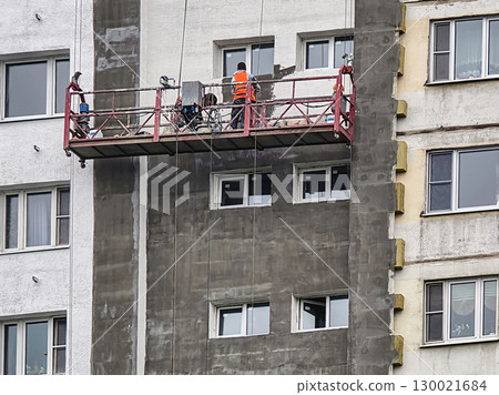 Workers repairing and insulating the exterior of a multi-story building in an urban area using a scaffold at midday Workers repairing and insulating the exterior of a multi-story building in an urban area using a scaffold at midday 130021684