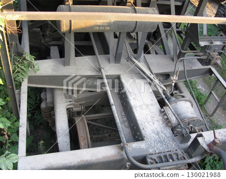 Close Up of a Train Undercarriage with Mechanical Components and Overgrown Vegetation 130021988