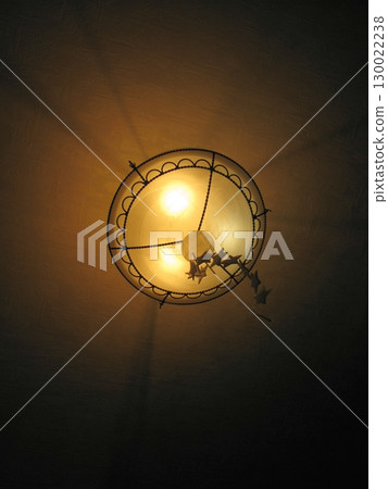 Glowing Ceiling Lamp with Ornate Design Casting Warm Light in a Dark Room 130022238
