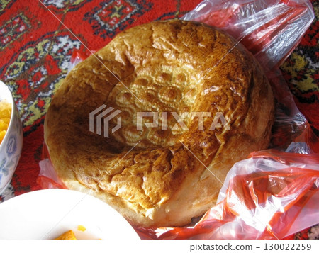 Round Bread Loaf with Patterned Top Wrapped in Plastic on a Patterned Rug 130022259