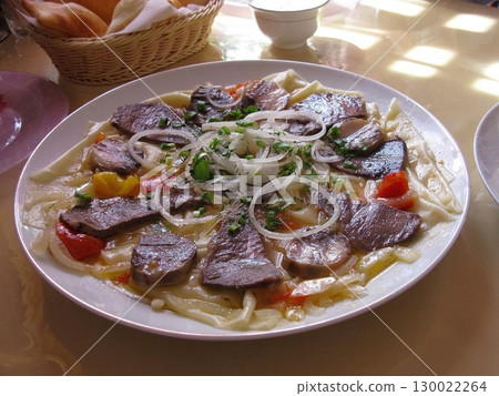 Large Plate of Pasta with Sliced Meat, Onions, and Peppers in a Dining Setup 130022264