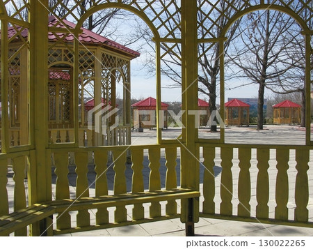 View of Multiple Gazebos with Red Roofs in a Park Through a Yellow Lattice Structure 130022265