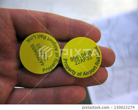 Hand Holding Two Yellow Tokens Marked as Property of an Airport Rail Link Hand Holding Two Yellow Tokens Marked as Property of an Airport Rail Link 130022274