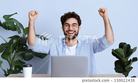 Cheerful young man male celebrating success with laptop in home office Cheerful young man male celebrating success with laptop in home office 130022438
