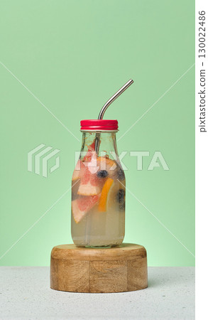Glass bottles filled with detox water infused with citrus slices and blueberries. Green background 130022486