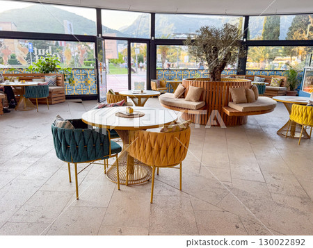 Modern cafe interior with stylish furniture and tree decor. Space reflects leisure, hospitality and urban lifestyle. 130022892