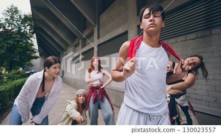 Male street dancer in white tank top posing with attitude while crew supports 130023557