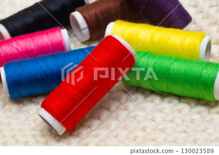 A set of colored threads for sewing on spools. A stack of multi-colored spools of thread 130023589