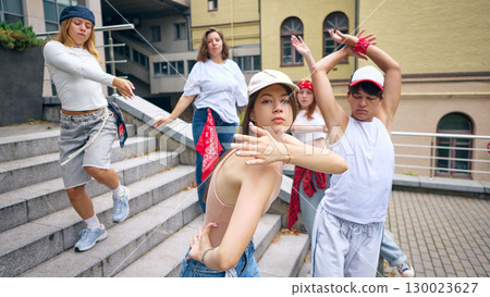 Female dancer in cap leading group with strong emotional expression on city stairs 130023627