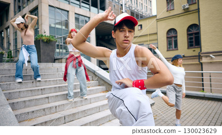 Young male street dancer in white outfit performing expressive move with confidence 130023629