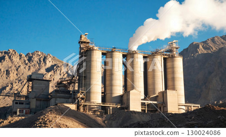 Industrial cement factory with smokestacks in rugged mountainous terrain 130024086