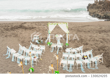 A beautiful beach wedding setup featuring elegant decor, lovely flowers, and a stunning ocean view 130024205