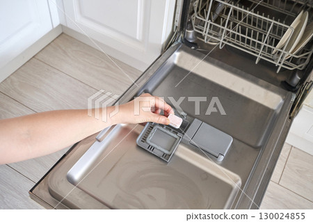 Woman loading dishwasher with detergent tablet in modern kitchen setting Woman loading dishwasher with detergent tablet in modern kitchen setting 130024855