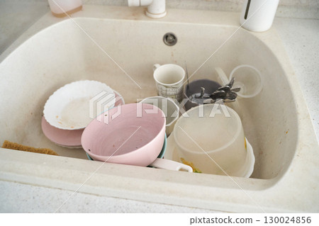 Dirty dishes in white kitchen sink with plates, mugs, and cutlery 130024856