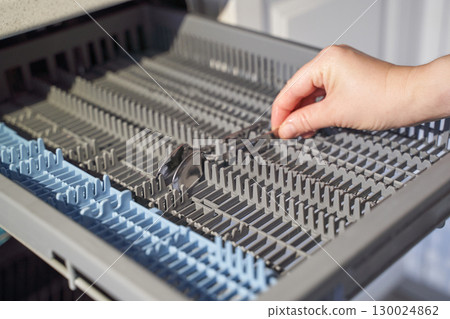 Caucasian adult hand loading silverware into dishwasher cutlery tray in modern 130024862