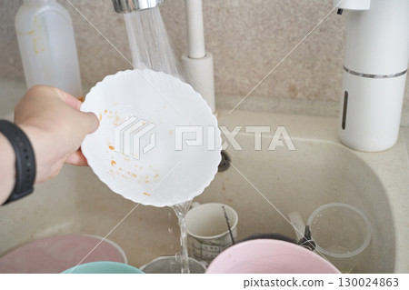 Caucasian female washing dishes under running water in kitchen sink with various Caucasian female washing dishes under running water in kitchen sink with various 130024863