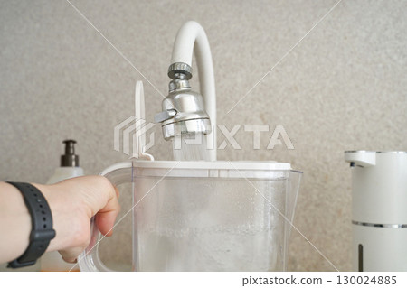 Hand filling water filter pitcher at kitchen sink with running faucet for clean 130024885