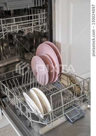 Open dishwasher with pink plates and white bowls in modern kitchen interior 130024897