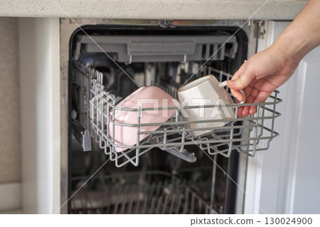 Female hand loading cups into dishwasher for cleaning in modern kitchen setting 130024900