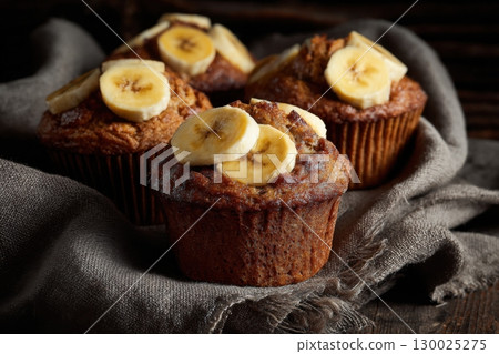 Banana cupcakes. Golden-brown freshly baked cupcakes topped with banana slices and brown sugar. Banana muffins on parchment paper against a rustic wooden background. Breakfast treat. Homemade dessert. 130025275