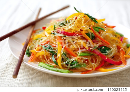 Cellophane noodles. White plate of salad with Glass Noodle and colorful vegetables, vibrant colors. Wooden chopsticks beside it, and orange sauce on top. Light beige background. Warm Asian salad 130025315